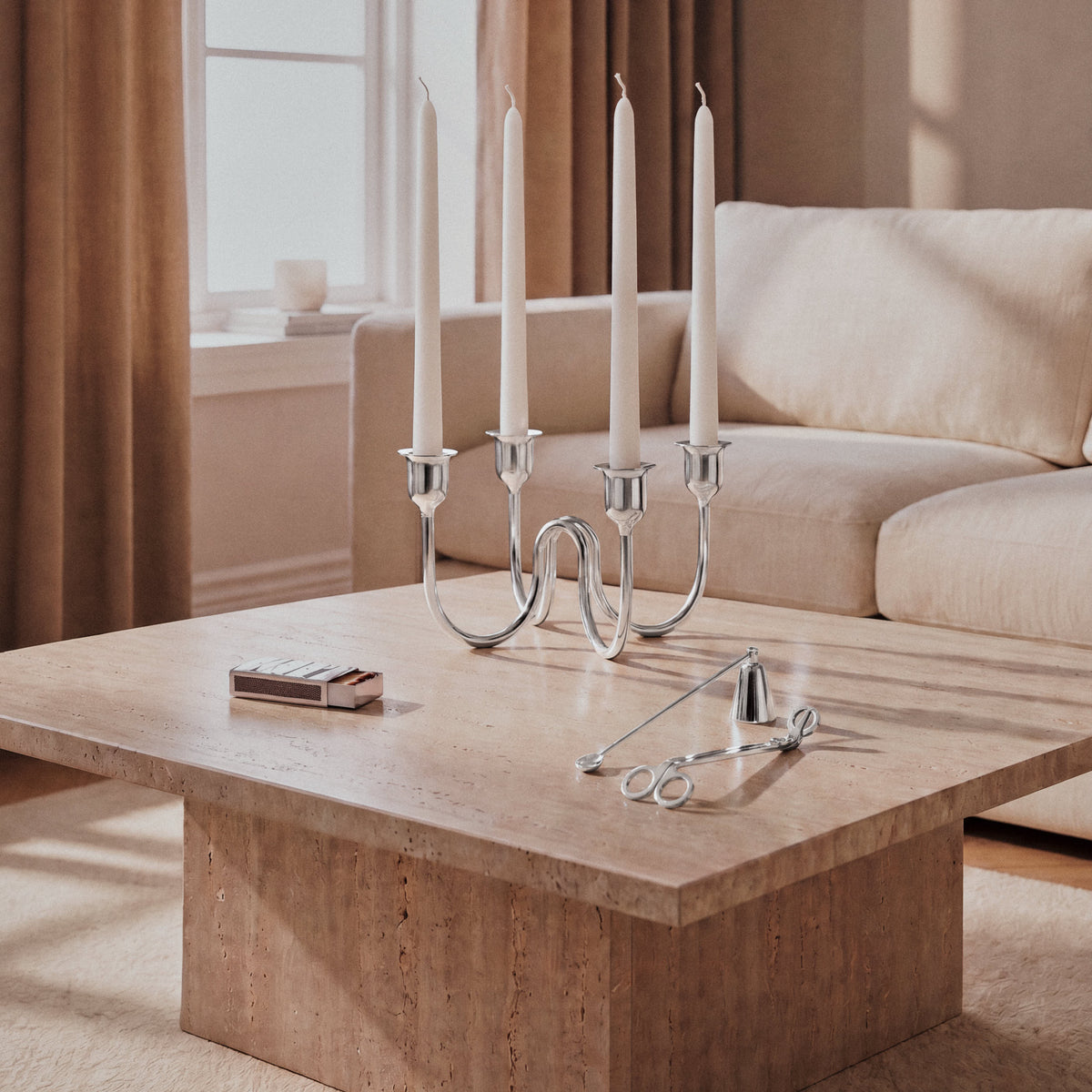 Silver-plated brass candelabra holding four white taper candles on a travertine coffee table in a living room.