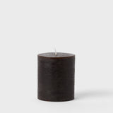 Hand-cast dark brown paraffin wax pillar candle against a plain light background.